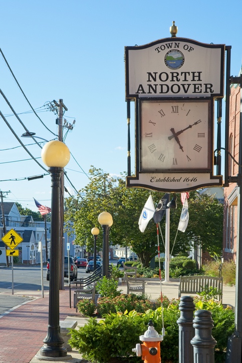 Town of North Andover, Established 1646 wooden clock sign along a tree-lined downtown street.