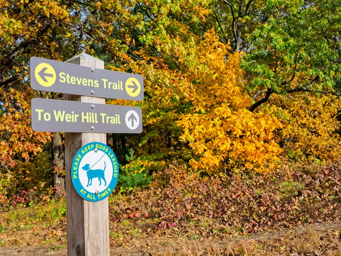 Trailhead signs marking Stevens Trail and the path to Weir Hill, surrounded by autumn foliage.