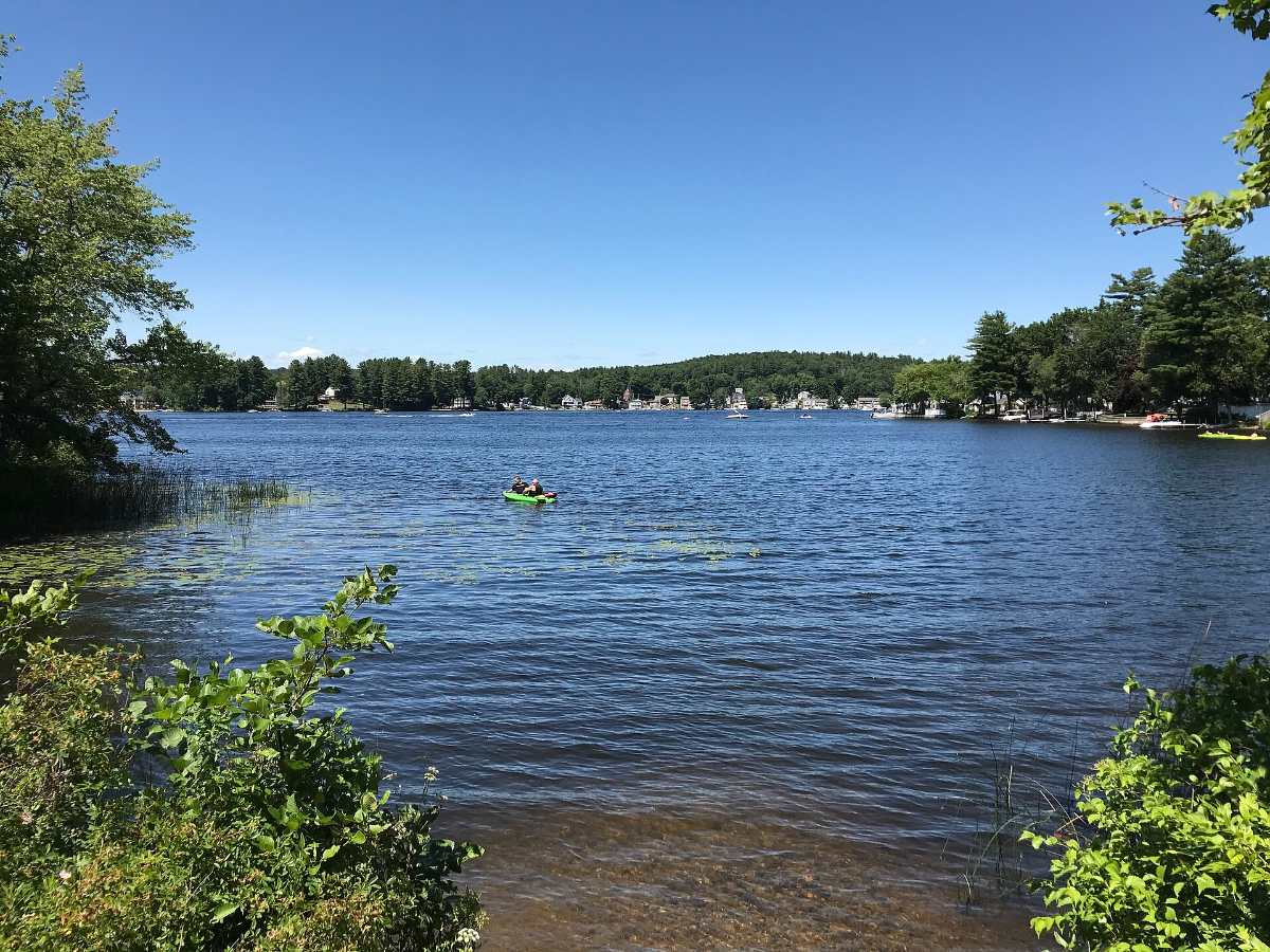 Beaver Lake on a clear summer day, with a kayak on the water, in Derry NH