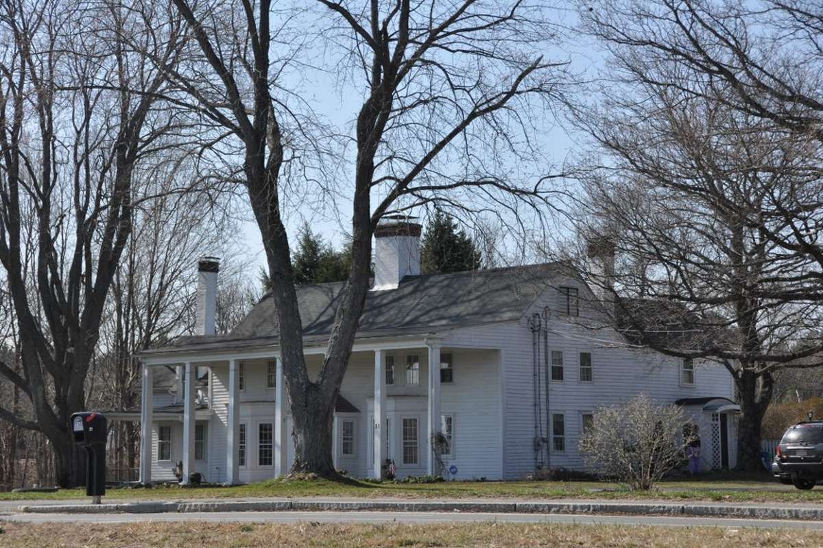 A white antique colonial with a columned porch under tall trees in Boxford MA