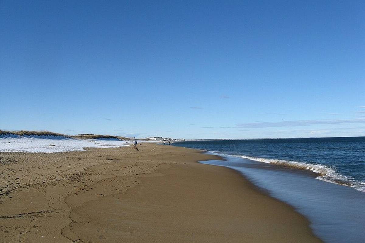 A wide sandy beach with gentle waves and light snow on the dunes in Salisbury MA